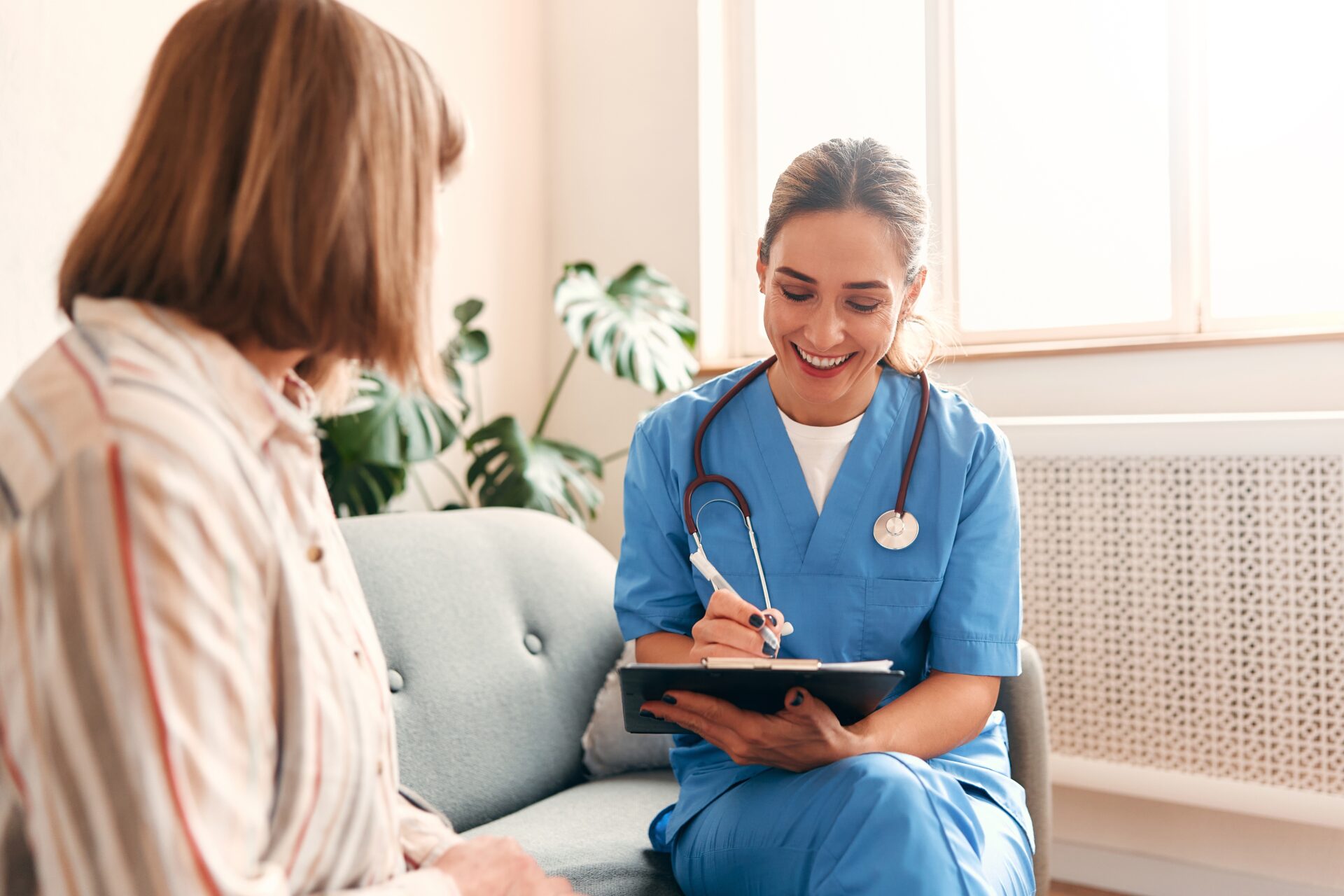 Happy,Young,Female,Nurse,Provide,Care,Medical,Service,Help,Support A health professional measures a woman's waist with a tape measure in a bright, modern consultation room filled with plants and healthy foods.